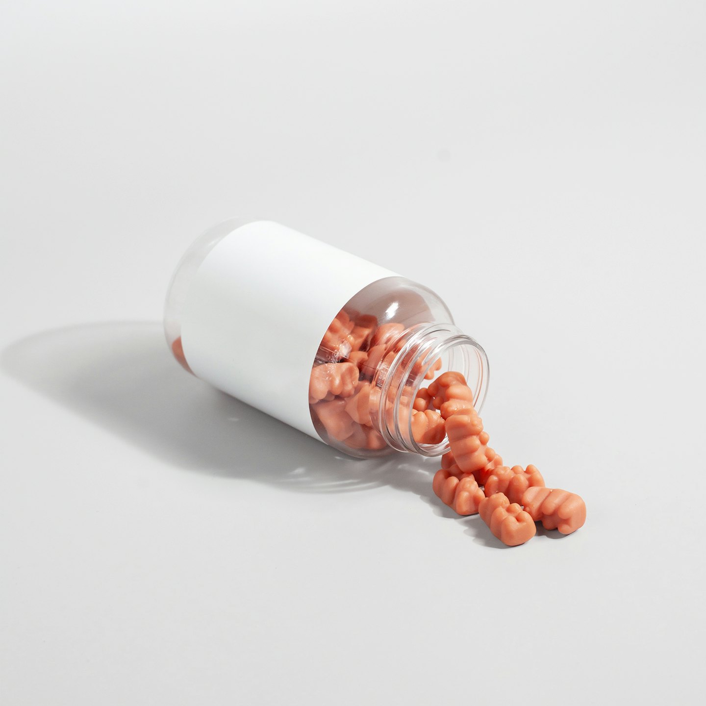 Orange gummy supplements spill from a plastic bottle on a white surface.